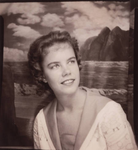 Photo booth portrait of a young woman with styled hair, posed with her head tilted, looking afar, wearing a jacket with long, triangular lapels
