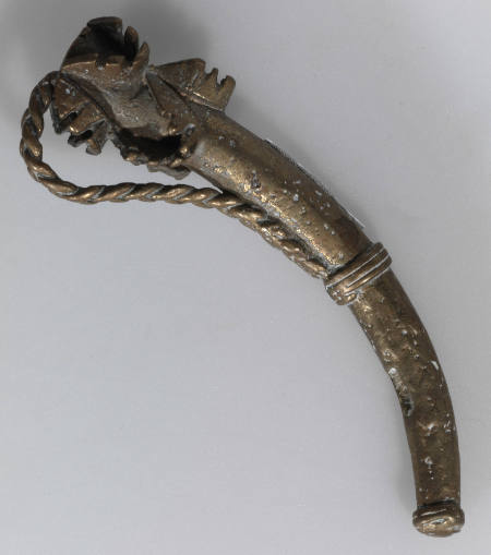 Goldweight in the form of a curved implement with a braided handle and protruding zig-zags
