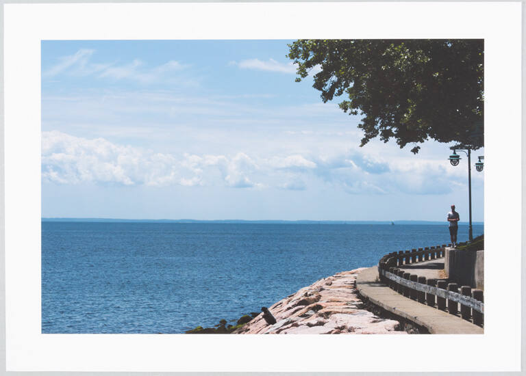 [Man standing by a lamppost near the water's edge]