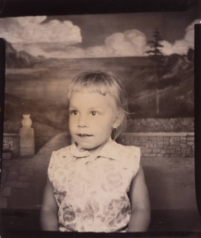 Photo booth portrait of a little girl with high, short bangs, wearing a sleeveless top