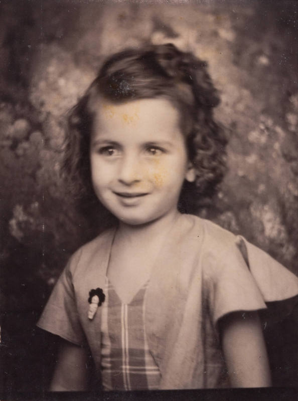 Photo booth portrrait of a small girl with curled, set hair, wearing a summer dress with a brooch