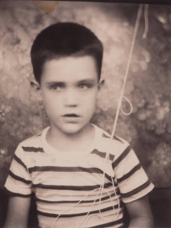 Photo booth portrait of a little boy with dark hair, wearing a shirt with horizontal stripes, looking to one side