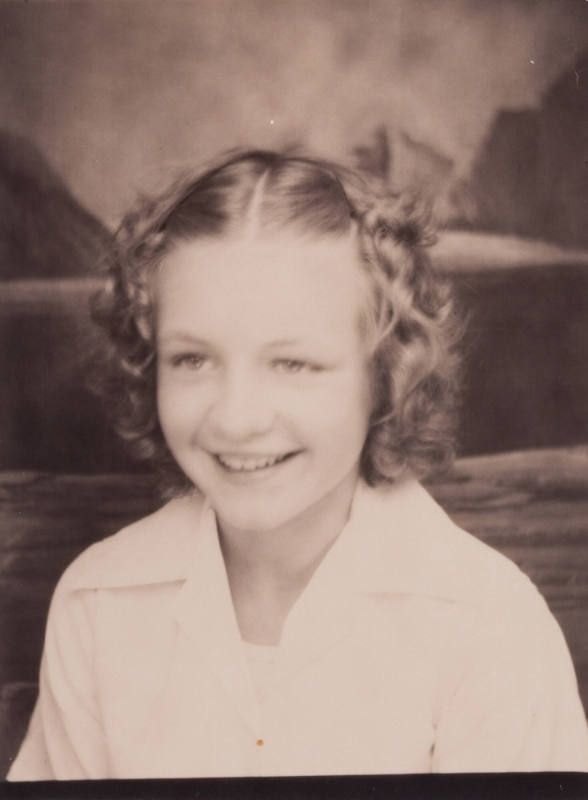 Photo booth portrait of a young girl with curly hair parted down the center, smiling or laughing