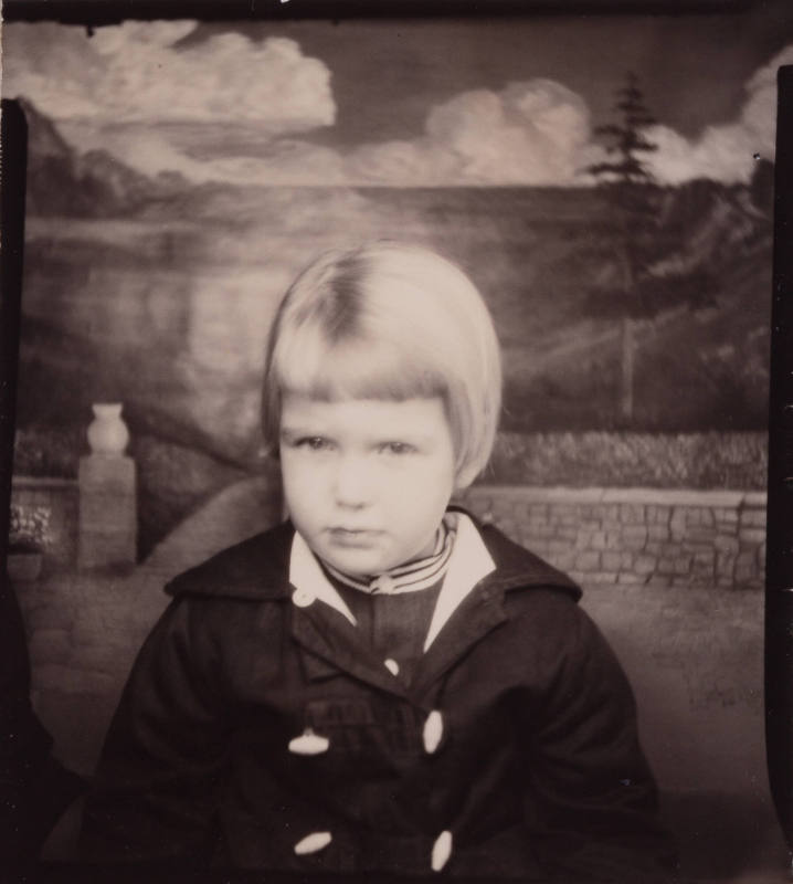 Photo booth portrait of a little girl with short, light-colored hair, wearing a peacoat