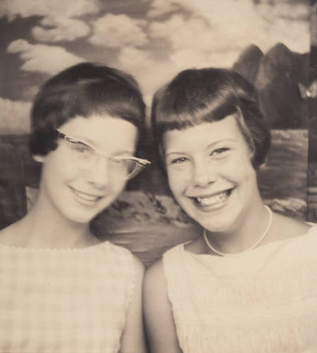 Photo booth portrait of two young girls, possibly sisters or twins, one wearing cat eye glasses and the other wearing a choker-style necklace