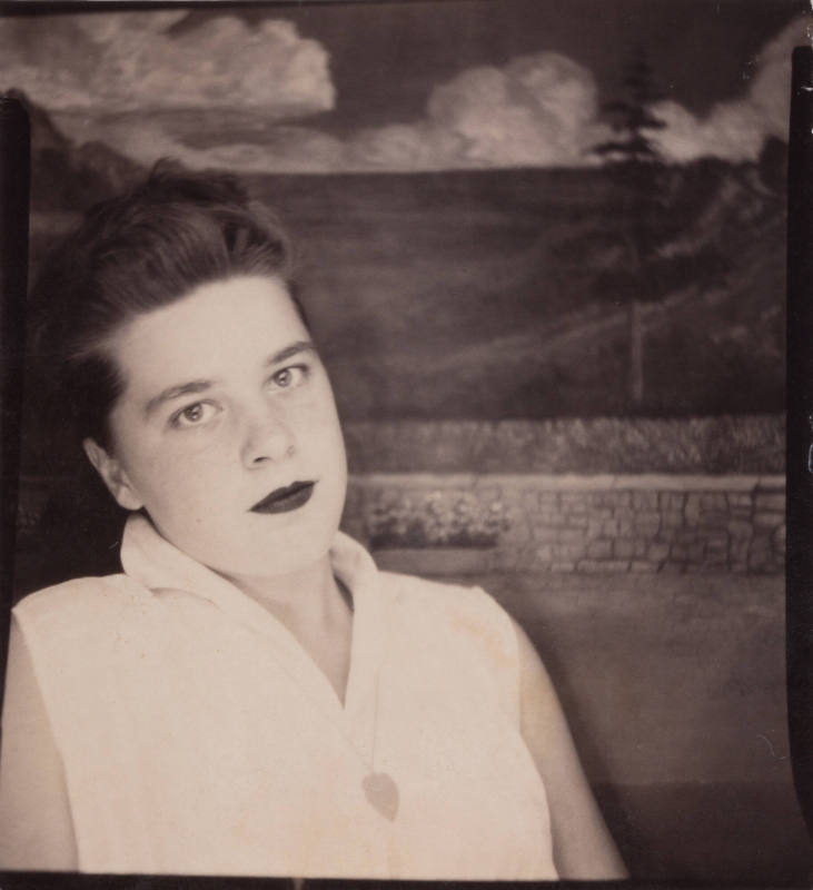 Photo booth portrait of a young woman with dark hair wearing lipstick and a sleeveless top, leaning back