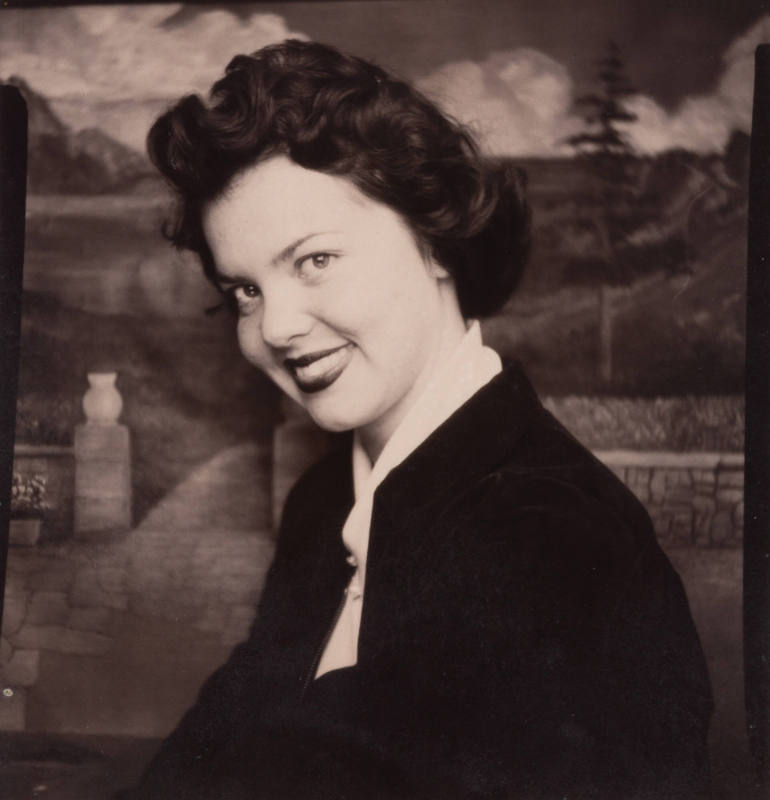 Photo booth portrait of a woman with styled hair, wearing a dark jacket and a light blouse