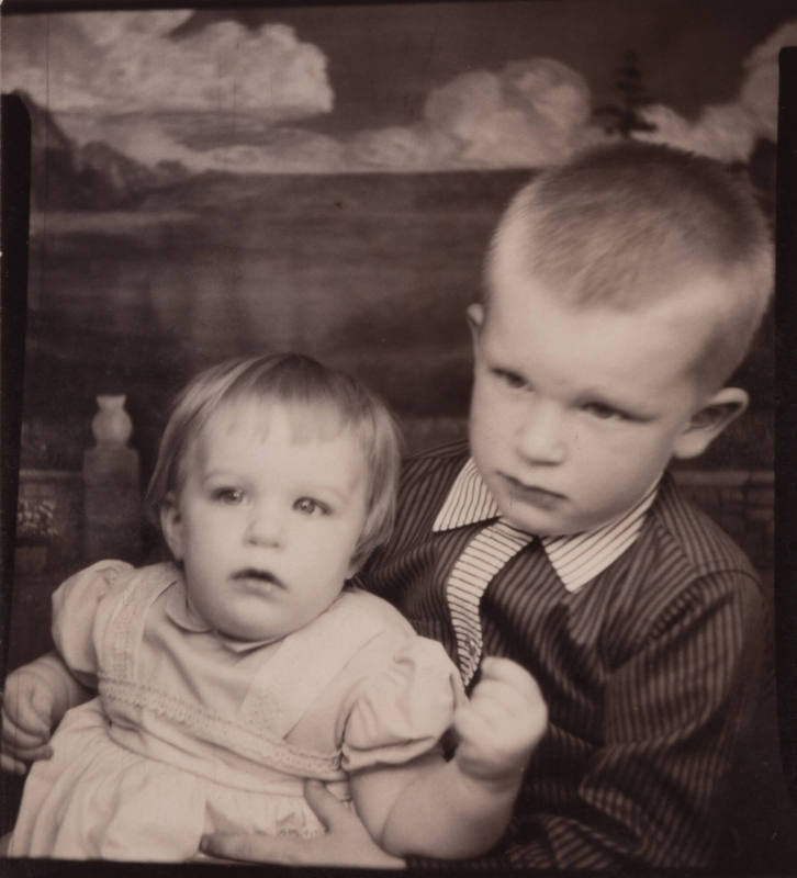 Photo booth portrait of a little boy and baby girl; the boy wears a shirt with striped collar and placket