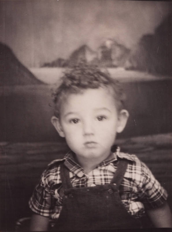 Photo booth portrait of a little boy with curly hair, wearing plaid shirt and overalls