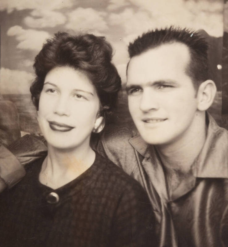 Photo booth portrait of a couple: the woman wearing lipstick and a brooch or clasp at her collar; the man wearing a satiny shirt with open collar
