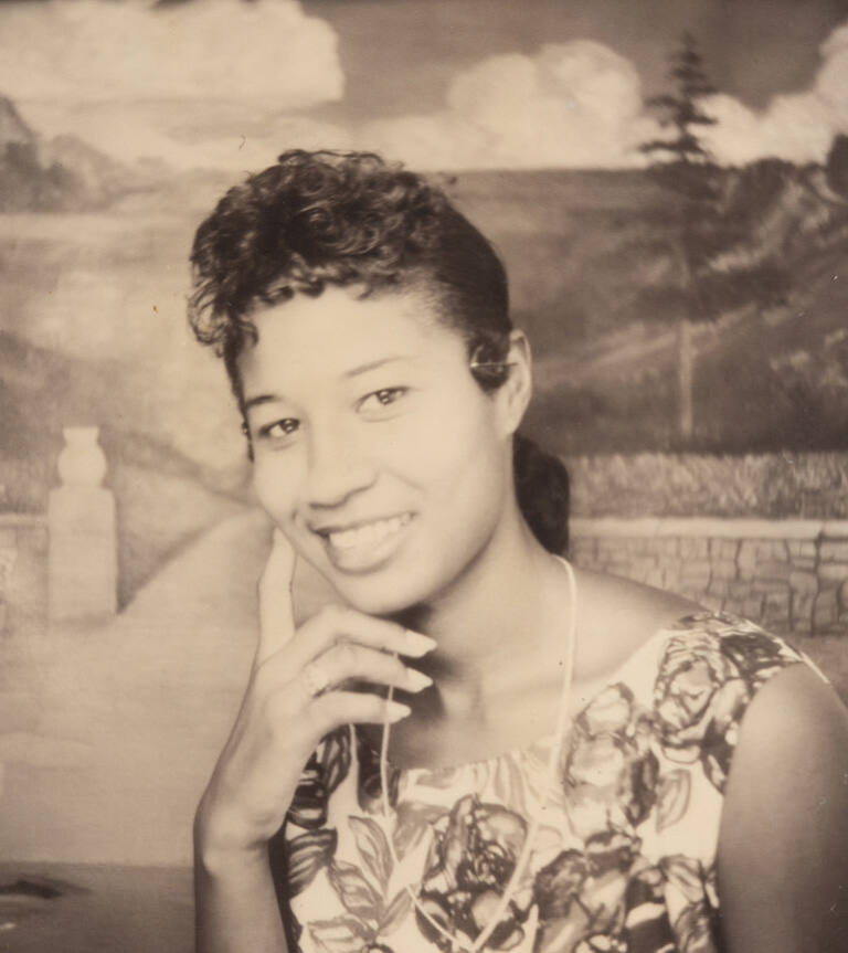 Photo booth portrait of a young woman wearing a floral dress or top, posed with her hand to her chin and one finger on her cheek