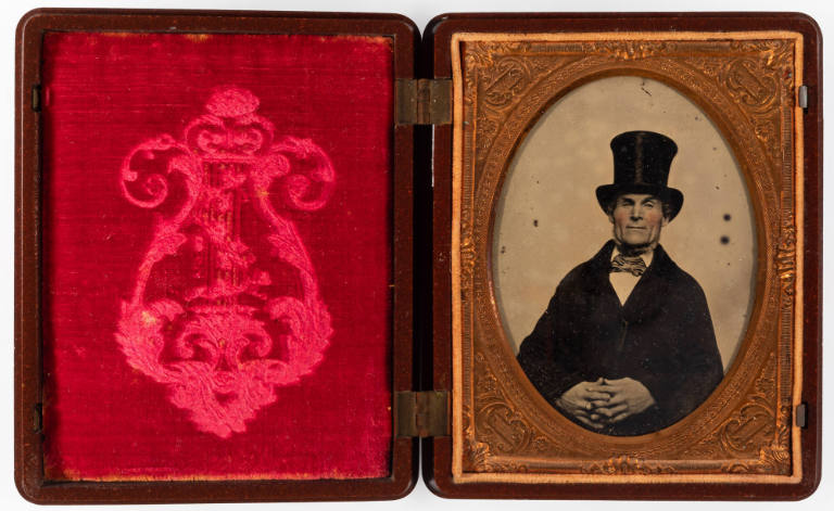 Untitled [Older man in top hat, hands clasped in lap, cheeks enhanced in red]