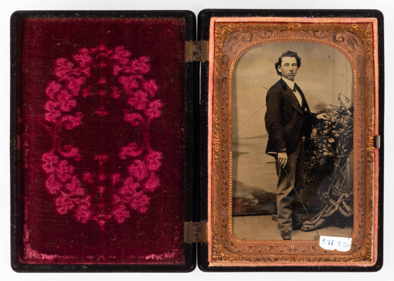 Untitled [Standing young man with riding crop, next to an elaborate display of flowers, cheeks enhanced with red]