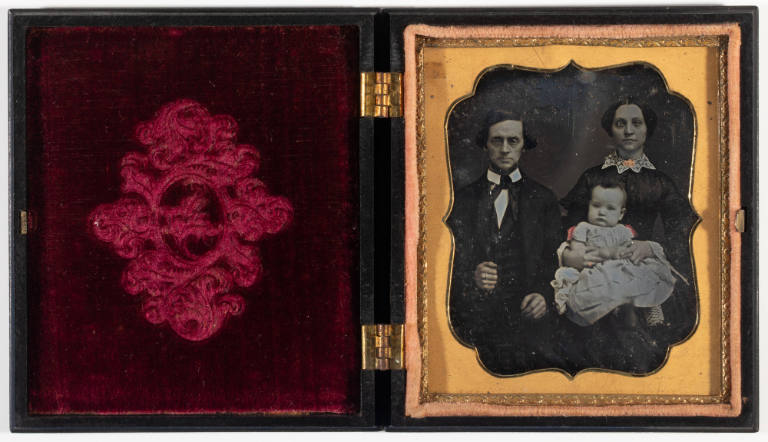 Untitled [Man and woman holding a baby, jewelry painted gold, bows on baby's dress painted red]