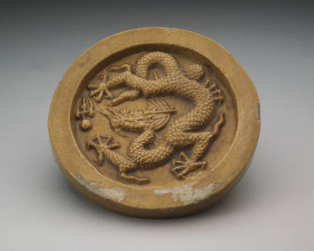 One of a pair of circular roof tiles with dragon design in high relief on circumferential wall.
