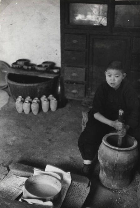 "Peiping Essay": Boy knocking on inside of vase to make it even inside a Cloisonné shop