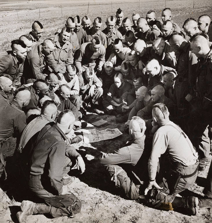 [U.S. Paratroopers with their hair cut in Mohawks for luck, are briefed for the next day's jump across the Rhine]