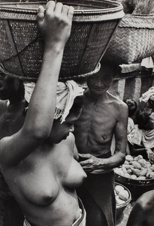 Bare breasted woman holding basket on head at market, Bali, Indonesia