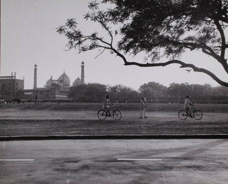 [People riding bicycles past Old Red Fort and Great Muslim Mosque, Delhi, India]