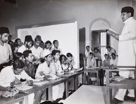 [Teacher addressing Pakistanti male students while female students are seated behind purdah wall in order to preserve their modesty, Sind Muslim College, Pakistan]