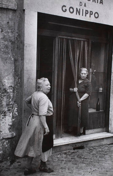 Woman holding beaded entrance curtain of "Trattoria Gonippo," Italy