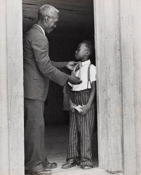 Sharecropper Lonnie Fair helps his son dress for Sunday school