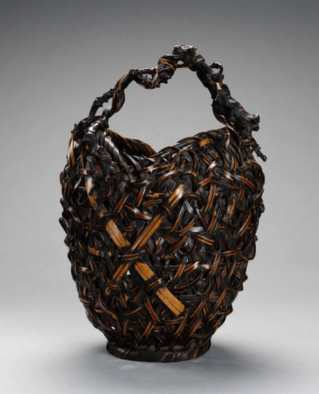 Basket composed of dark and light colored, coarse materials, and having natural twig or vine handle