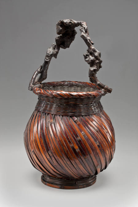 Basket with diagonally-patterned weave on the body, and a "knotty" or "burled" handle made of natural twig or vine