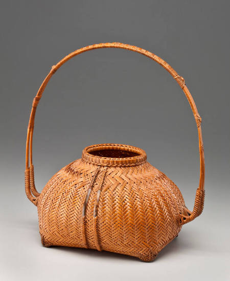 Light colored basket with handle parts that project horizontally from the body, then arc above the body, forming a broad loop