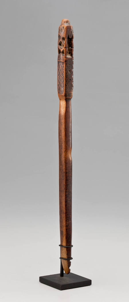 Wooden staff with figure at top, head in hands, "x" motif carved into wood