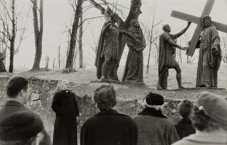 Priest standing in front of statues speaking to a group of pilgrims, Lourdes