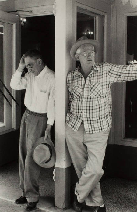 Two men leaning against white post, USA